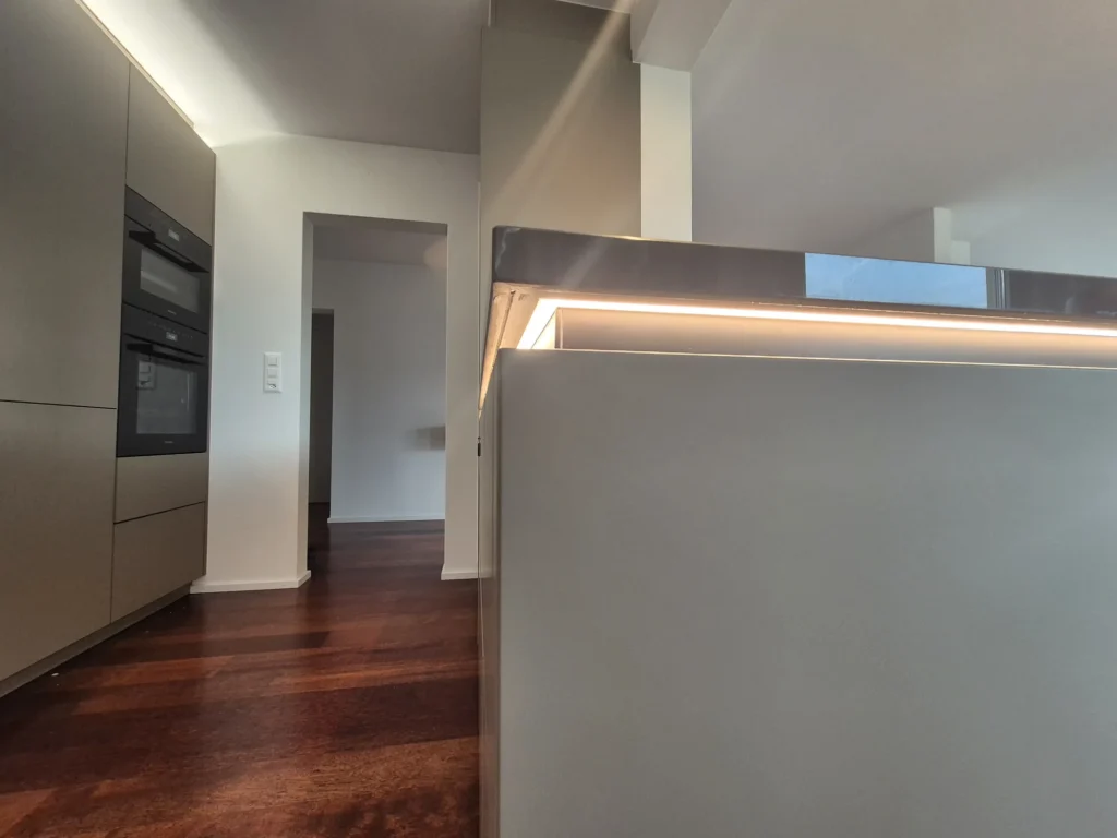 Kante der Arbeitsplatte mit Lichtband, im Hintergrund ein Hochschrank mit Backöfen