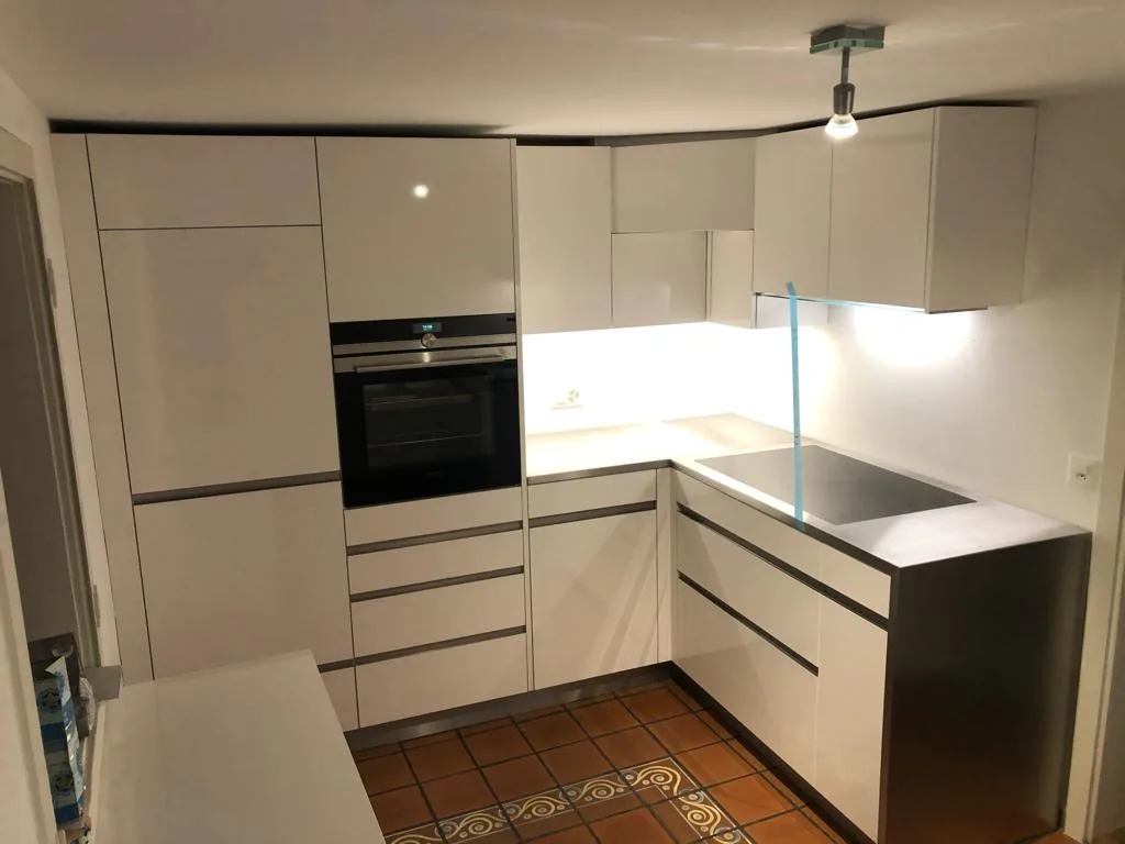Helle Eckküche mit Backofen und beleuchteter Arbeitsfläche auf einem Boden aus Tonplatten
