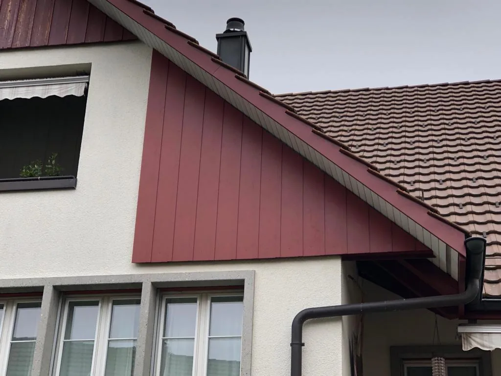 Giebel mit roter Holzverkleidung an einem Haus mit Ziegeldach