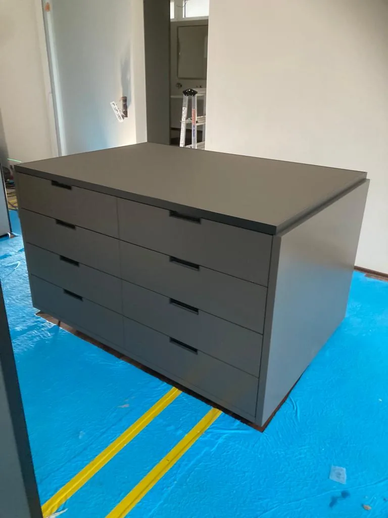 Graue Kommode mit Schubladen und dunkler Abdeckung auf abgedecktem Boden