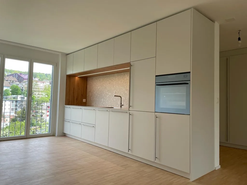 Helle Schrankwand mit Nische aus Holz, Spüle und Backofen neben bodentiefen Fenstern