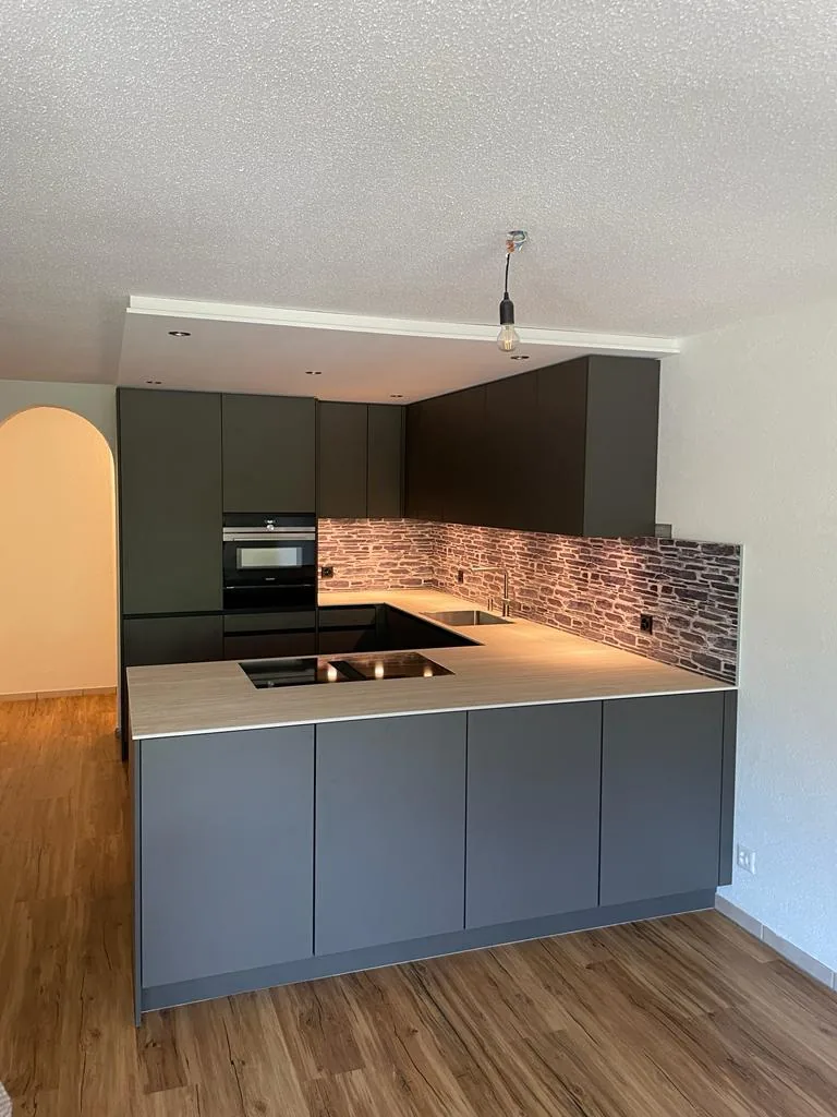 Dunkle Küche in U-Form mit Rückwand in Steinoptik und Holzboden