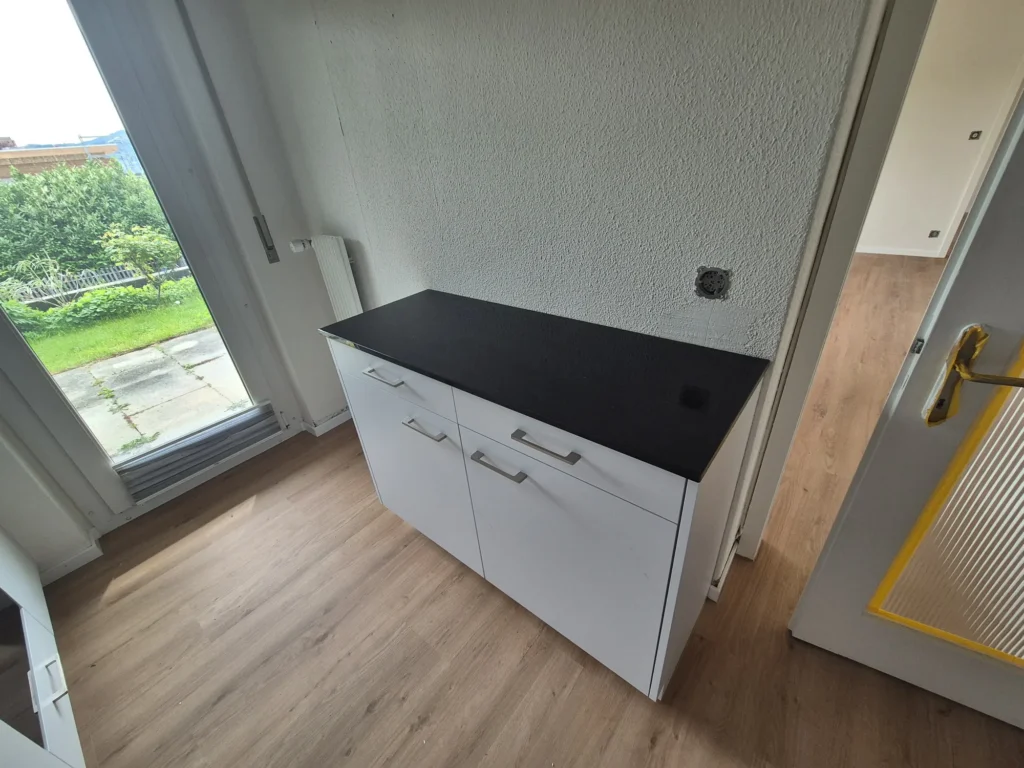 Weisser Unterschrank mit schwarzer Abdeckung neben einem bodentiefen Fenster